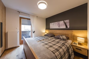 A bedroom with a large bed, a nightstand with a lamp, a radiator, and a window with curtains. - LUXURY APARTMENT in Mallnitz with Sauna - A (Mallnitz)