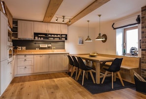 A modern kitchen with wooden cabinets, a central island with chairs, pendant lighting, and a brick wall. - LUXURY APARTMENT in Mallnitz with Sauna - A (Mallnitz)