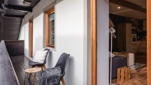 Ein gemütlicher Balkon mit Holztisch, zwei Stühlen und einem kleinen Hocker.