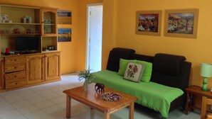 A living room with a green sofa, wooden cabinets, a television, and artwork on the walls.