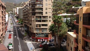 A multi-story building with balconies, a street in front, and a mountainous backdrop.