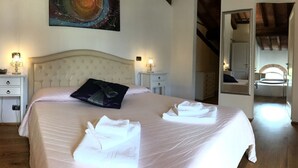 Un lit bien fait, avec du linge de lit et des serviettes blanches, une tête de lit, des tables de chevet avec des lampes et un tableau au mur.