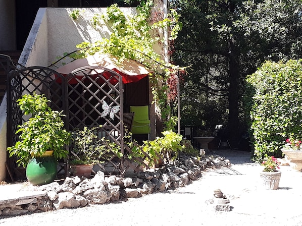 Un jardín con pérgola, plantas en macetas y un muro de piedra.