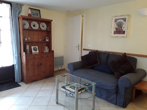 Una sala de estar con un sofá azul, una mesa de centro de vidrio y un aparador de madera con platos.