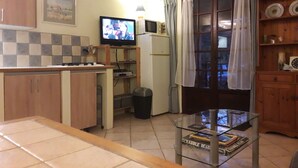Una cocina compacta con televisión, un refrigerador pequeño y una mesa de vidrio con libros.