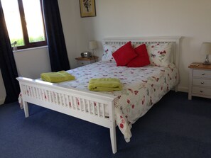 A bedroom with a white bed, floral bedding, two red pillows, and two green towels.