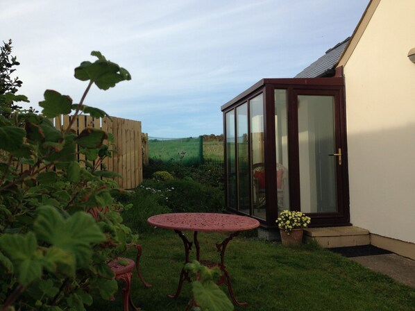 A garden with a wooden fence, a glass door, a round table, and a chair.