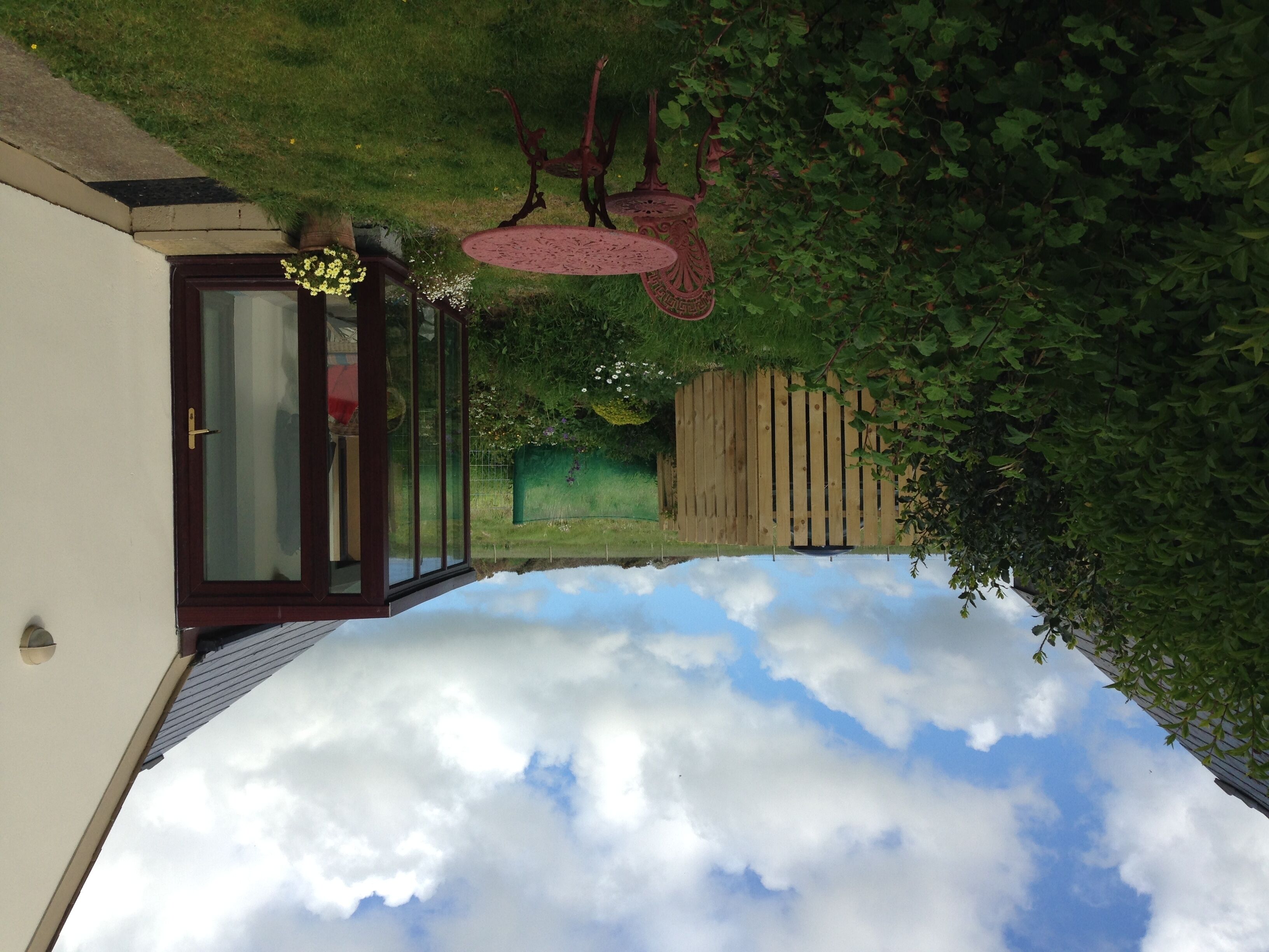 A room with a view of the sky through a glass door, a wooden fence, and a garden area.