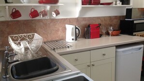 Una cocina con un lavamanos, hervidor, hervidor rojo, tazas rojas y un microondas.