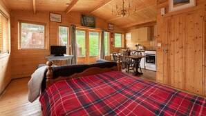 Una cabaña acogedora con colcha escocesa, paredes de madera, zona de comedor y cocina.