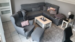 Una sala de estar moderna con un sofá seccional gris, una mesita blanca, un sillón negro y una alfombra gris.