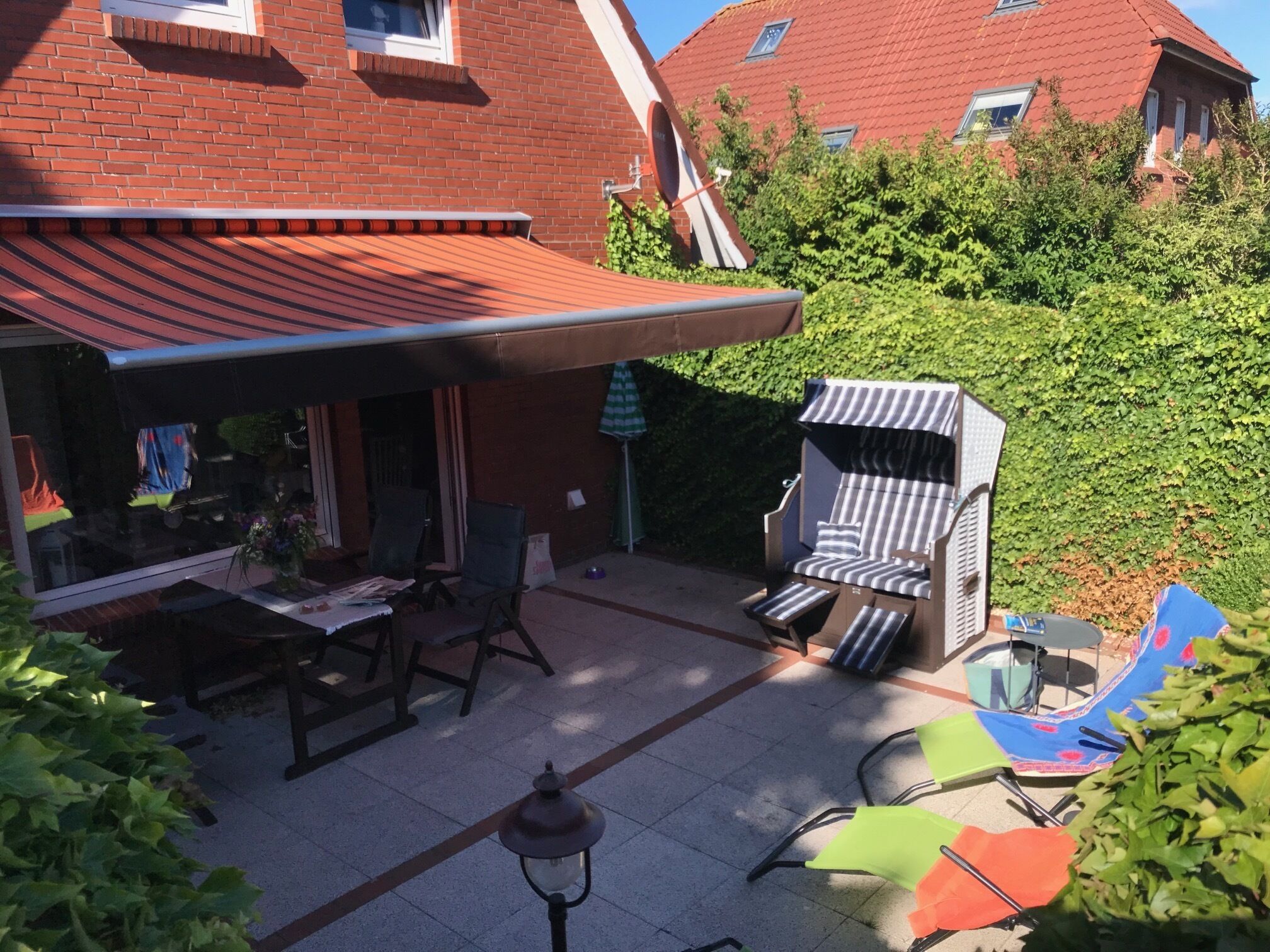Patiolla on pöytä ja tuoleja, pieni oleskelualue, jossa on raidallinen koristetyyny, sekä valaisinpylväs.