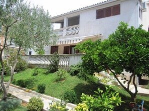 A two-story building with a balcony, surrounded by well-maintained greenery and a paved pathway.