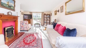 A living room with a fireplace, a sofa, a television, and a bookshelf. - Clovelly Cottage - Four Bedroom Cottage, Sleeps 8 (Crantock)