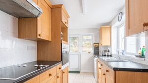 A kitchen with wooden cabinets, a black countertop, a stainless steel sink, and a window with a view of trees. - Clovelly Cottage - Four Bedroom Cottage, Sleeps 8 (Crantock)
