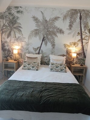 A bed with a green bedspread, two nightstands with lamps, and a wall with a tropical mural.