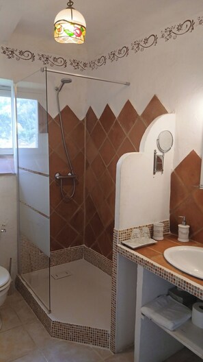 A bathroom with a glass shower enclosure, a sink with a mirror, and a decorative light fixture.
