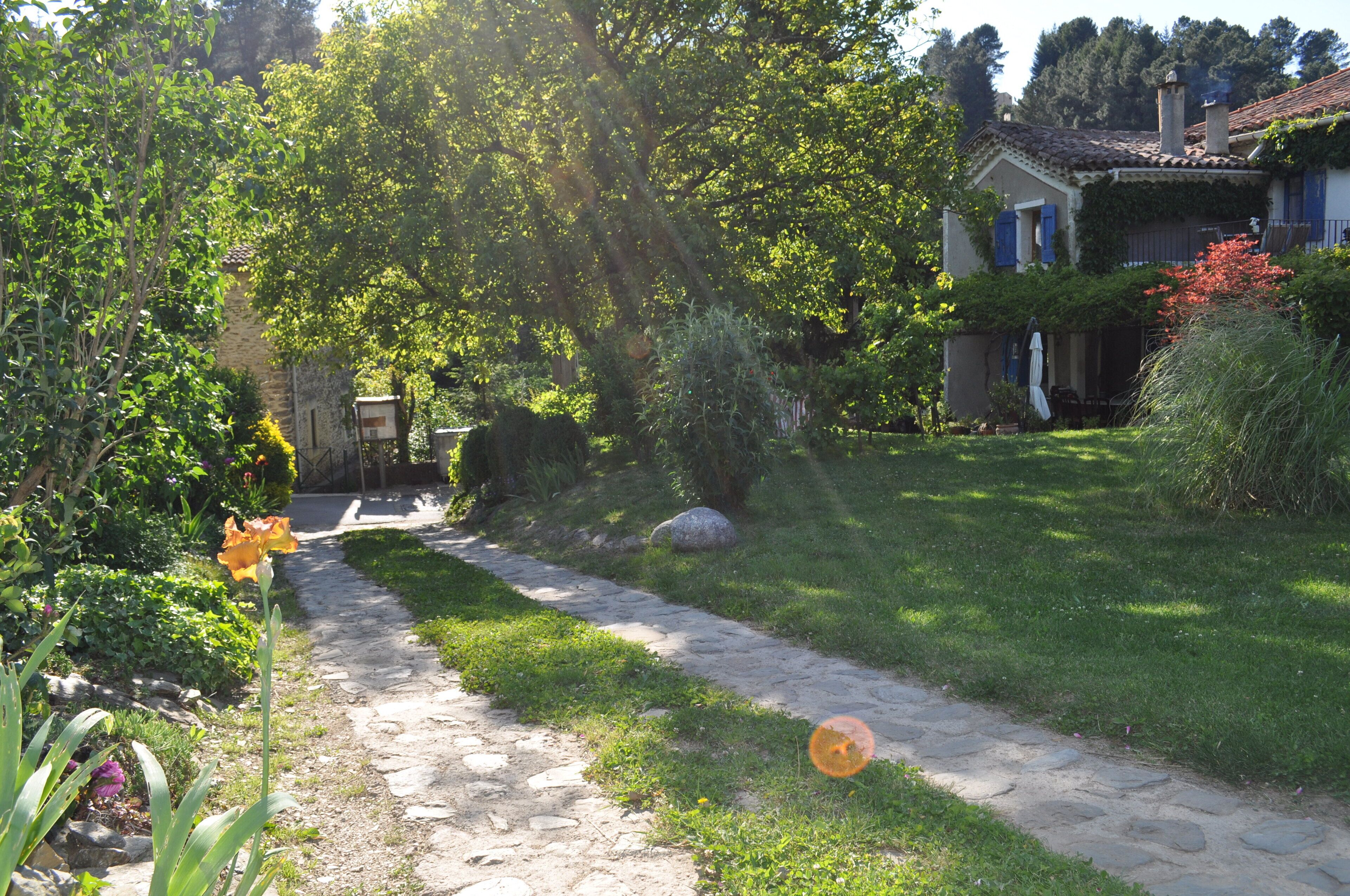 Ein gepflasterter Weg führt zu einem Haus mit einem Ziegeldach, umgeben von üppigem Grün und einem Garten.