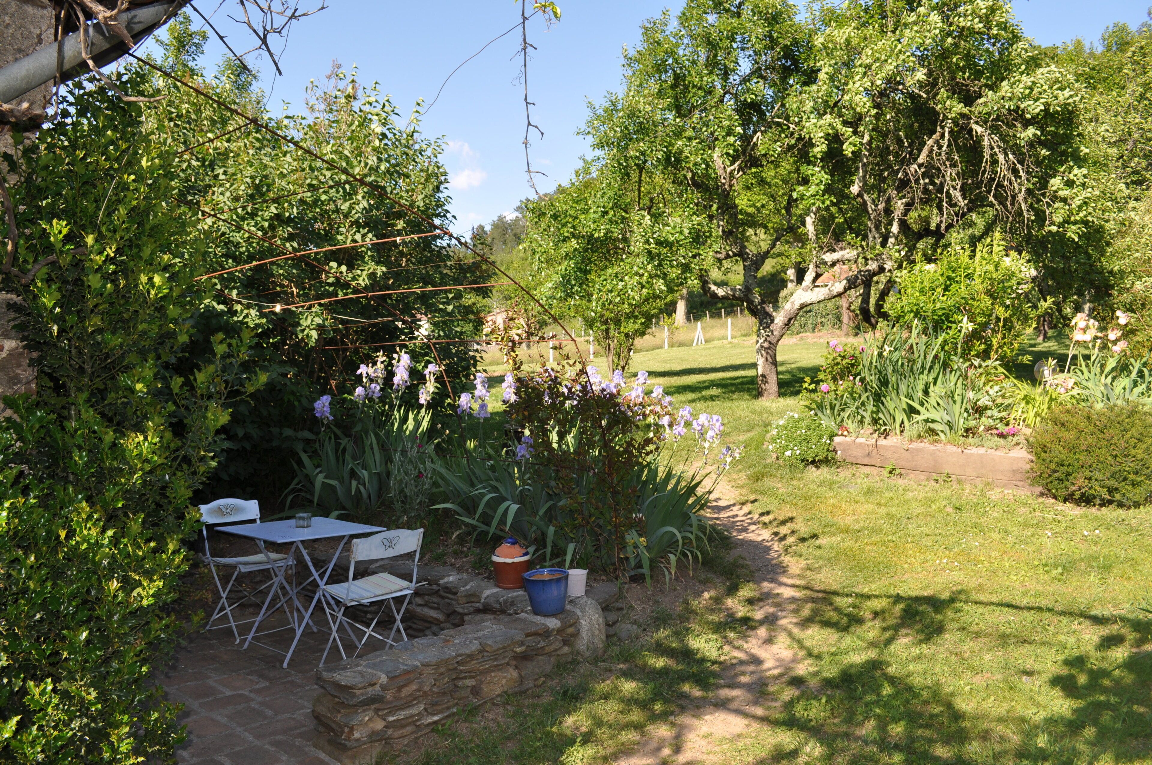 A garden with a stone table and chairs, surrounded by lush greenery and flowering plants.