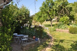 A garden with a stone table and chairs, surrounded by lush greenery and flowering plants.