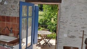 Et rustikt køkken med vask, træbordplade og en blå dør, der fører til en udendørs terrasse med et bord og stole.
