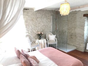 Ein Schlafzimmer mit einem Bett, einem Schminktisch mit Spiegel, einem Sessel und einer Duschkabine aus Glas.