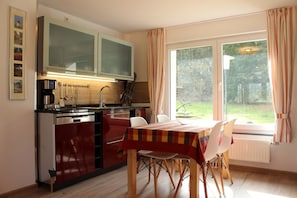 A compact kitchen with a dining area, featuring a coffee maker, a sink, and a window with curtains.