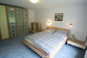 A bedroom with a large bed, wooden wardrobe, bedside tables, and wall-mounted lights.