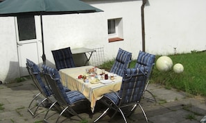 A patio with a table set for four, surrounded by striped chairs, a small window, and a green umbrella.