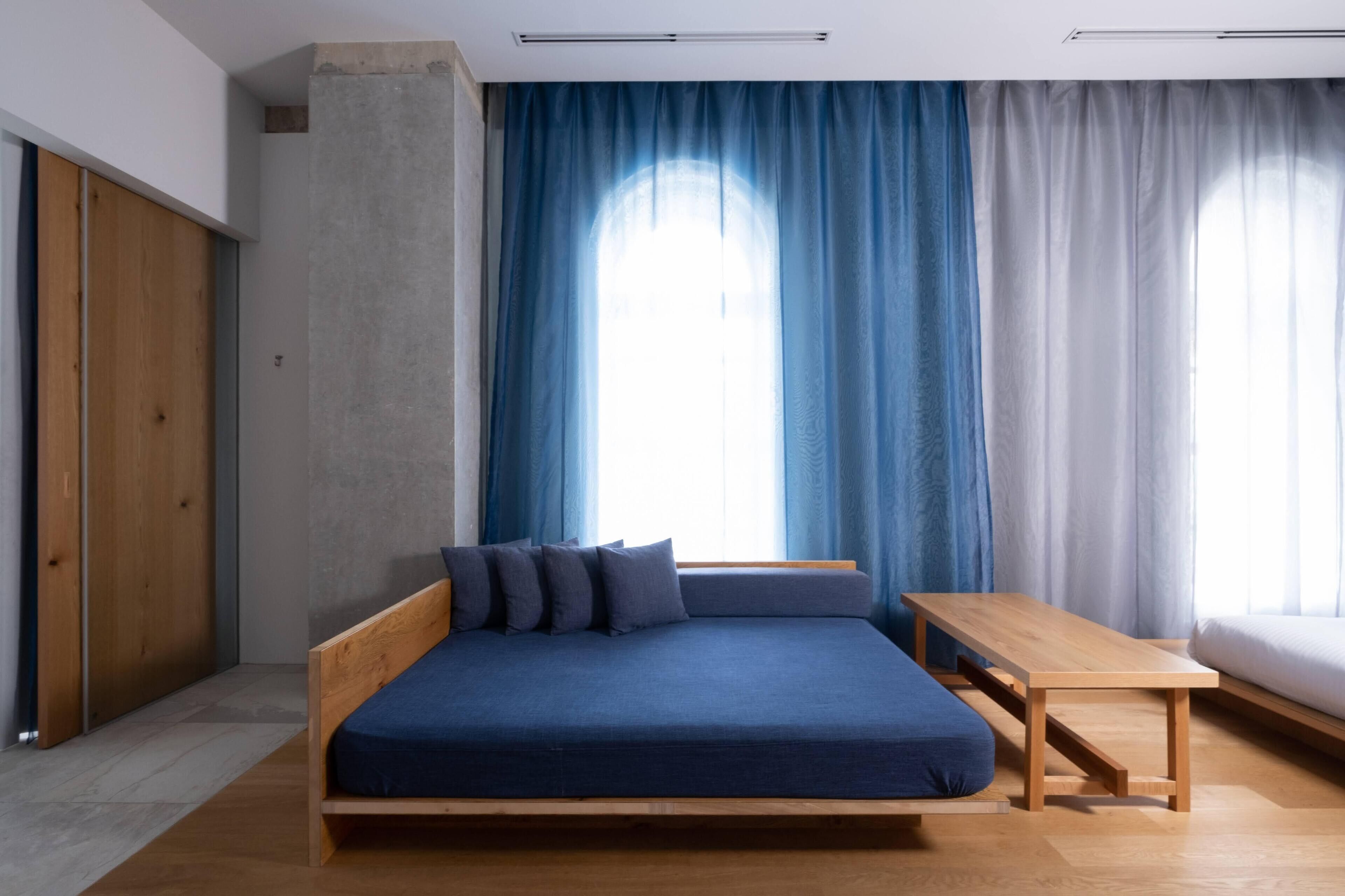 A modern bedroom with a wooden bed, a small wooden table, and a large window with blue curtains.