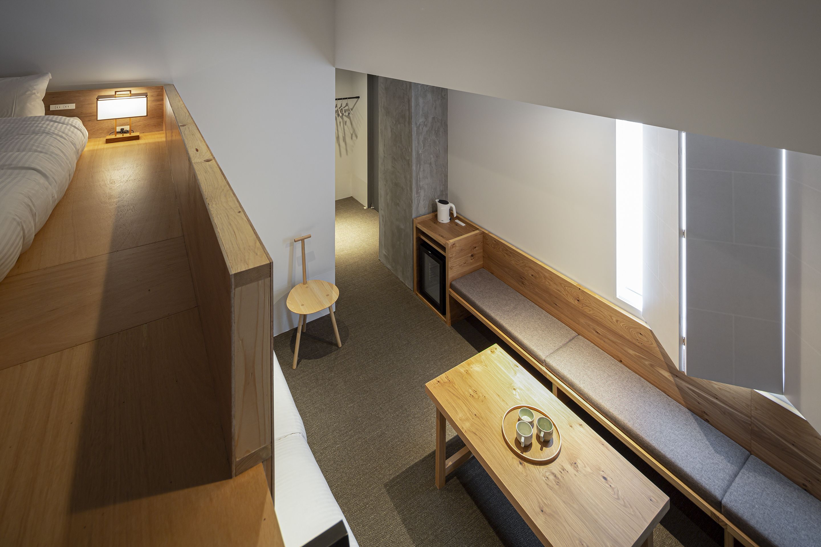 Ein kleines Zimmer mit einem Bett, einem Tisch mit Tassen, einer Bank und einem Fernseher.