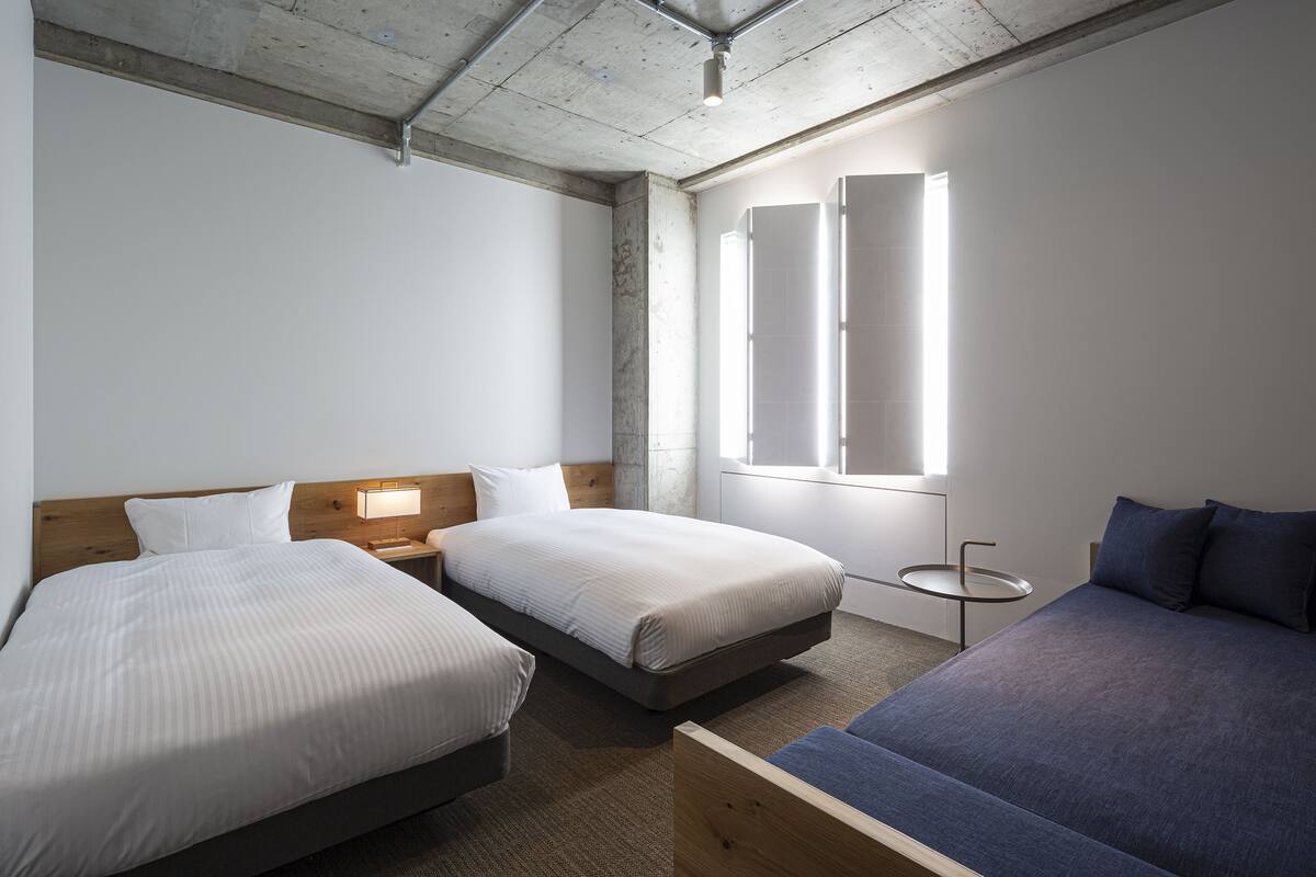 Ein Hotelzimmer mit zwei Betten, einem kleinen runden Tisch und einem Fenster mit Jalousien.