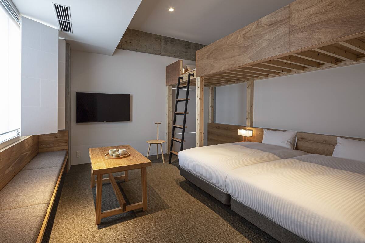 Ein modernes Hotelzimmer mit Schlafkoje, einem kleinen Tisch mit Tasse, einer Bank und einem an der Wand befestigten Fernseher.
