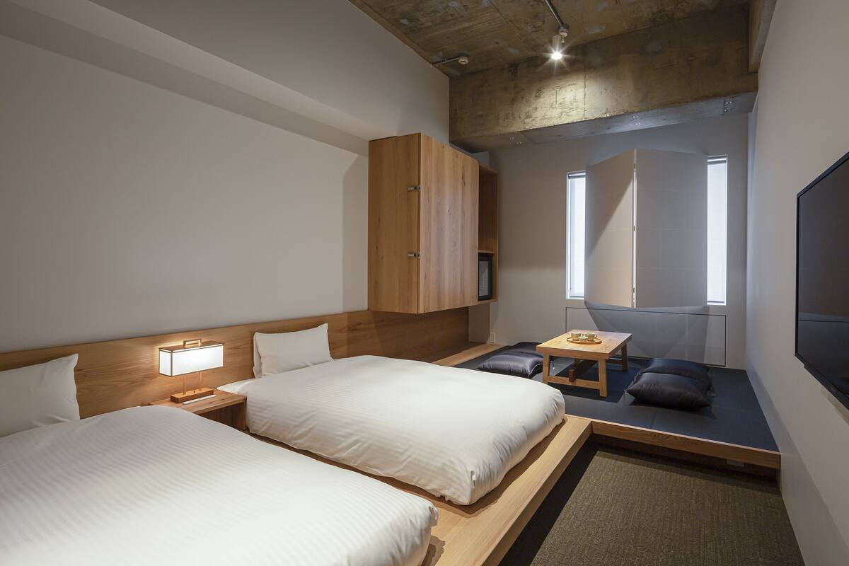 Ein modernes Hotelzimmer mit zwei Betten, einem Holzschrank, einem kleinen Tisch und einem Fernseher.