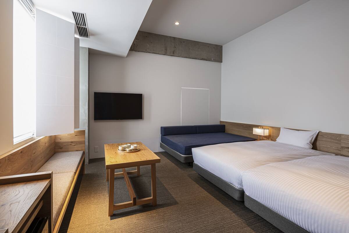 Ein modernes Hotelzimmer mit einem großen Bett, einer Couch, einem kleinen Tisch mit Tassen und einem an der Wand befestigten Fernseher.