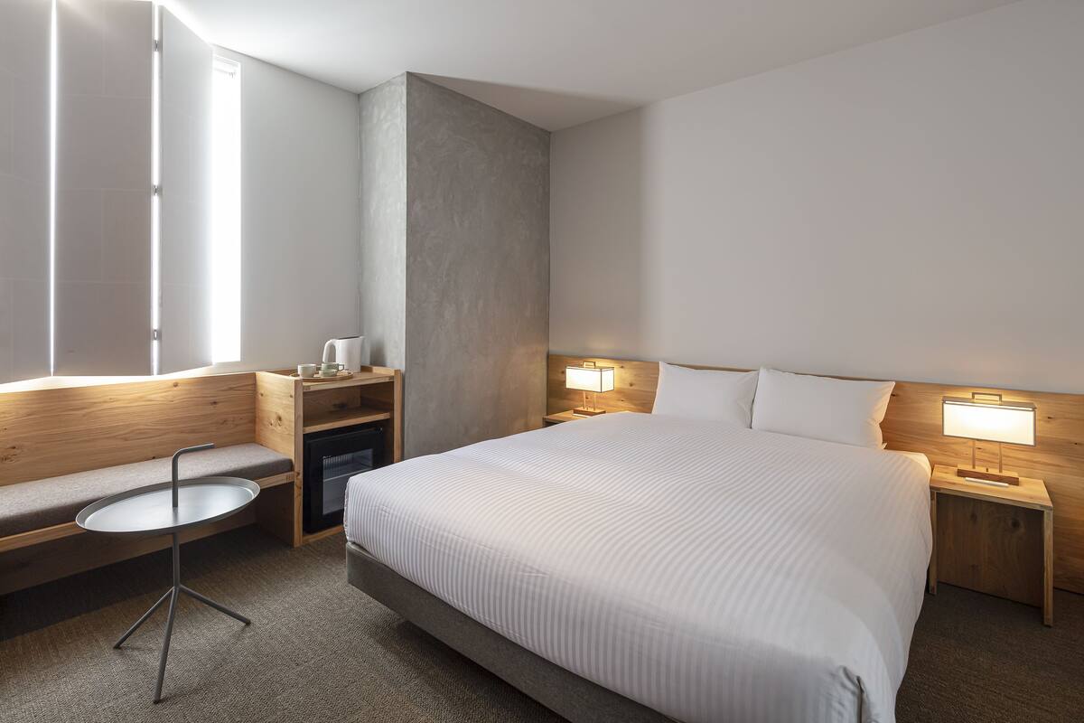 Ein Hotelzimmer mit einem großen Bett, einem kleinen runden Tisch, einer Bank und zwei Nachttischen mit Lampen.