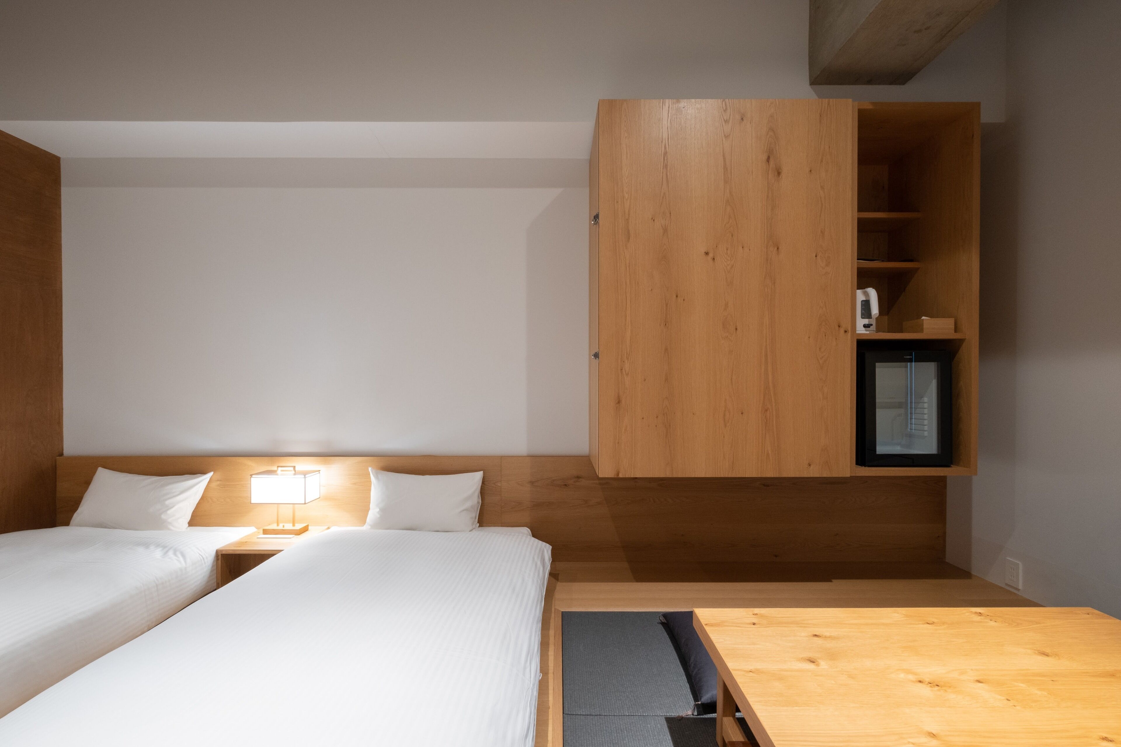 Ein Schlafzimmer mit zwei Betten, einem Holzschrank, einem Nachttisch mit Lampe und einem kleinen Regal mit Fernseher.