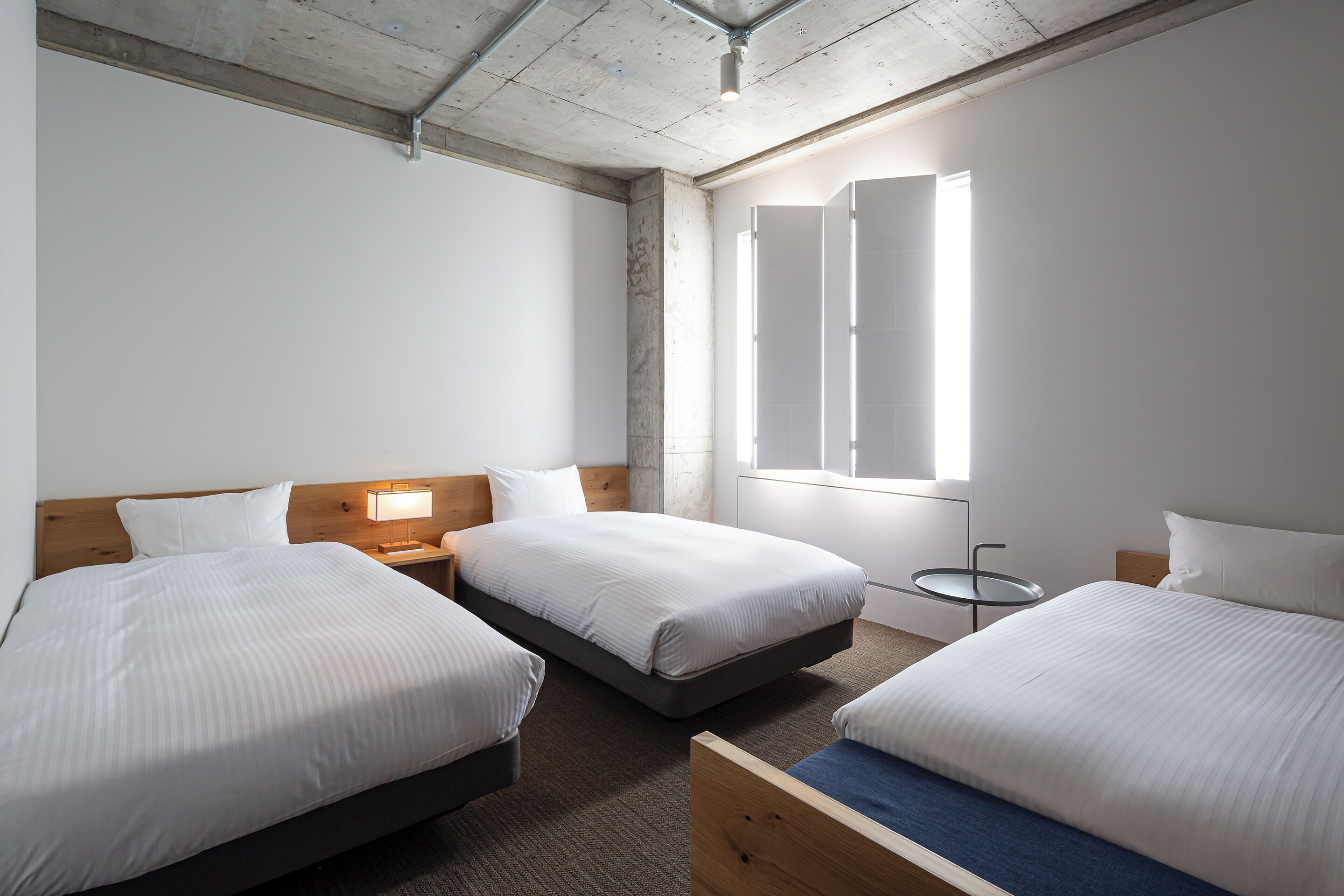 A hotel room with three beds, a small round table, and a window with blinds.