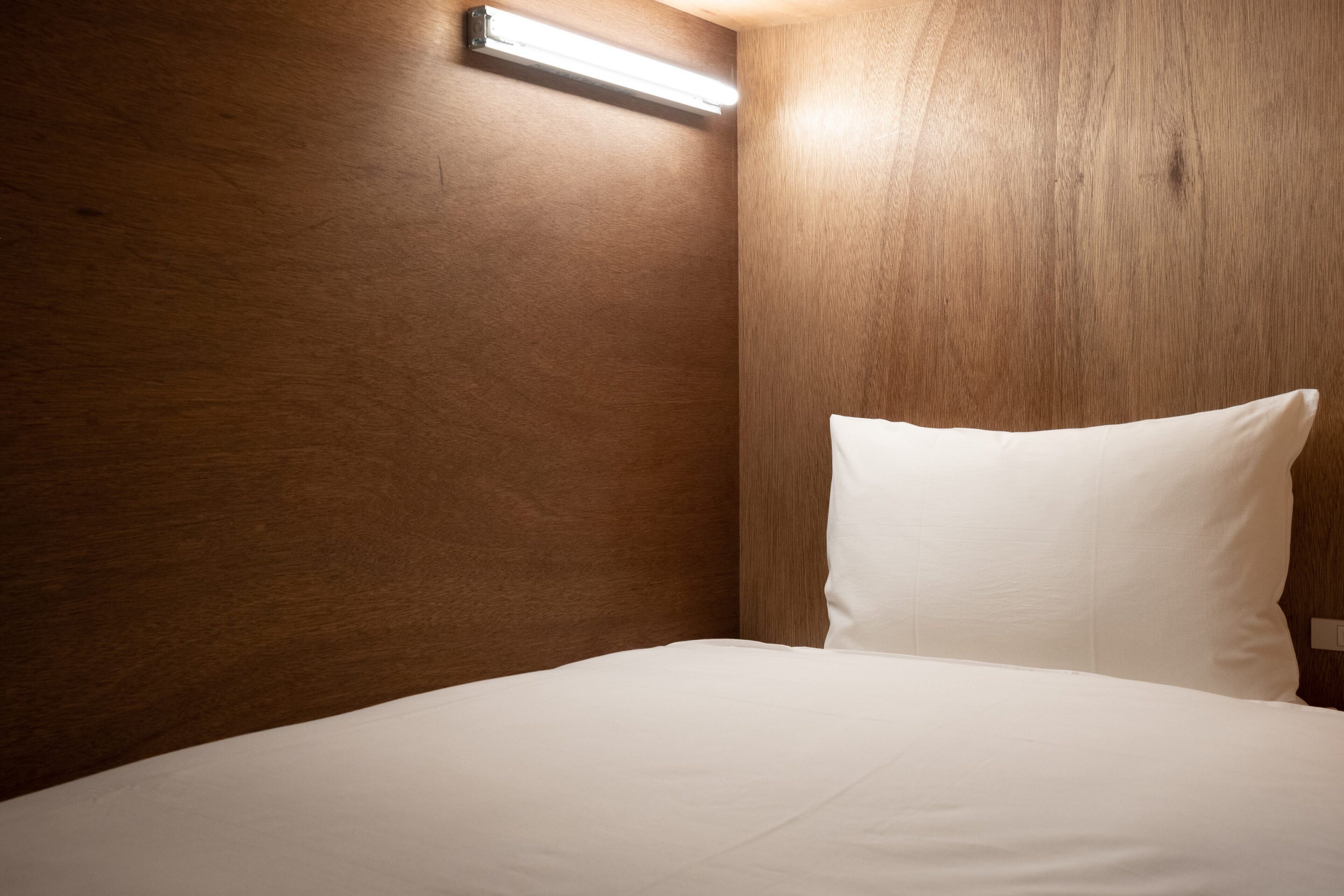 Une chambre d’hôtel avec un mur en bois, un lit avec une literie blanche et un luminaire fixé au plafond.