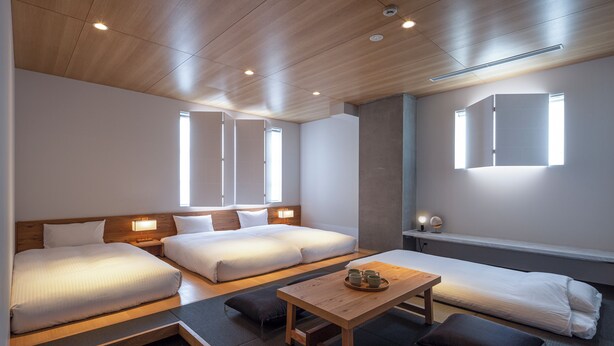 A hotel room with a wooden ceiling, two beds, a small table with cups, and a window.