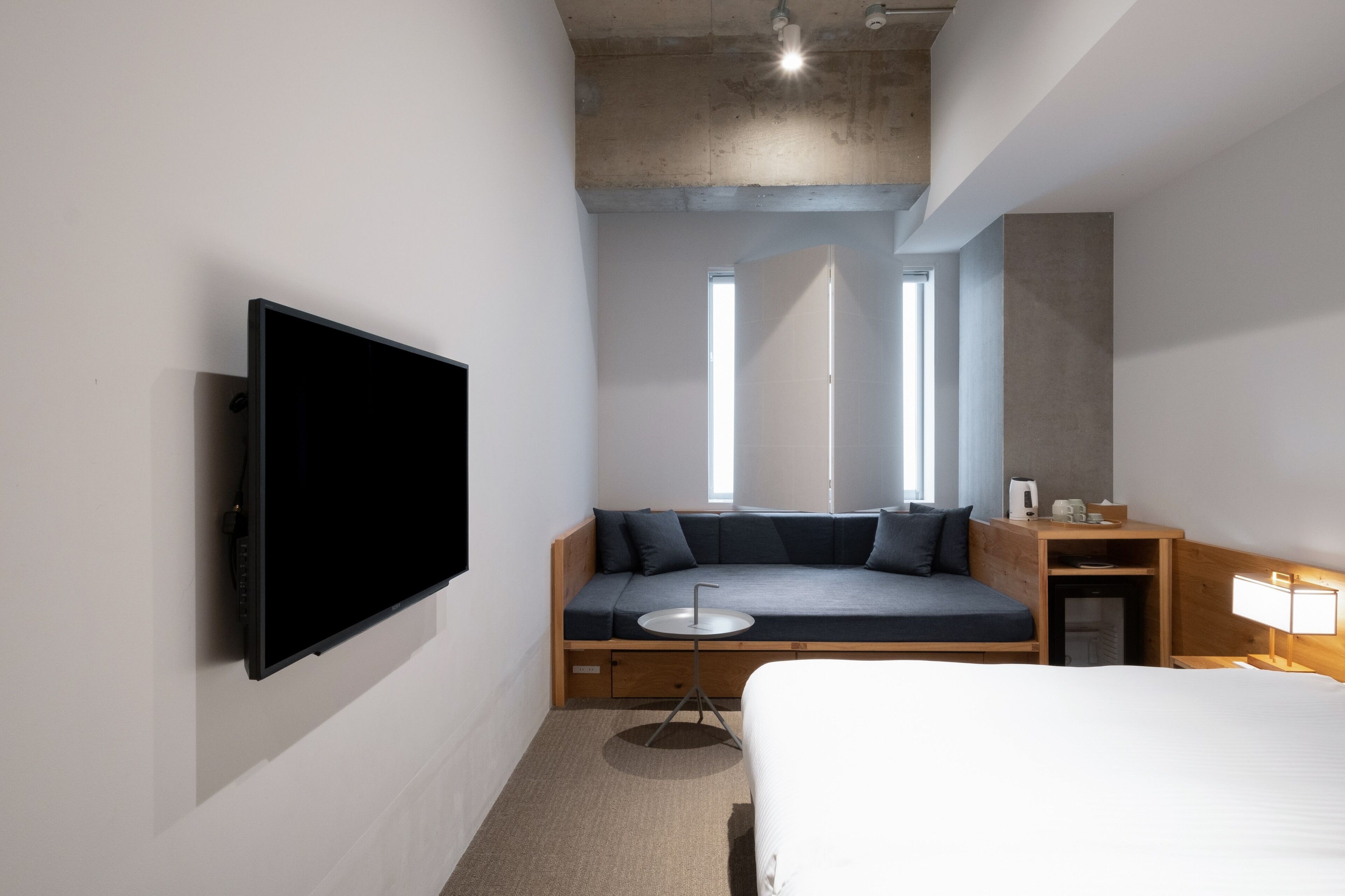 Une chambre d’hôtel moderne dotée d’un grand lit, d’un téléviseur à écran plat fixé au mur, d’un coin salon avec des coussins et d’une petite table.