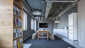 A modern office space with a wooden bookshelf, a table with a cactus, and a kitchen area with white cabinets.