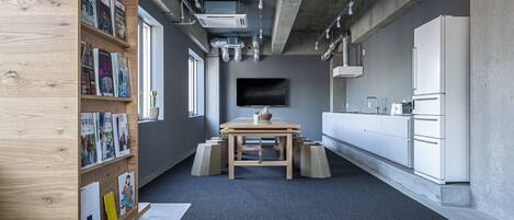 A modern office space with a wooden bookshelf, a table with a cactus, and a kitchen area with white cabinets.