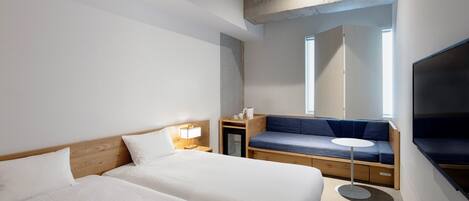 A hotel room with two beds, a sofa, a small table, a TV, and a window.