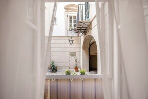 Un patio estrecho con un balcón, plantas en macetas y una lámpara tradicional.