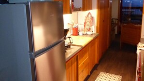 Una cocina con armarios de madera, un refrigerador de acero inoxidable, una encimera con varios objetos y una alfombra estampada en el suelo.