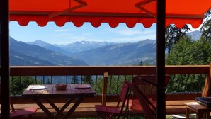 Terraza de madera con mesa y sillas, con vistas a un paisaje montañoso.