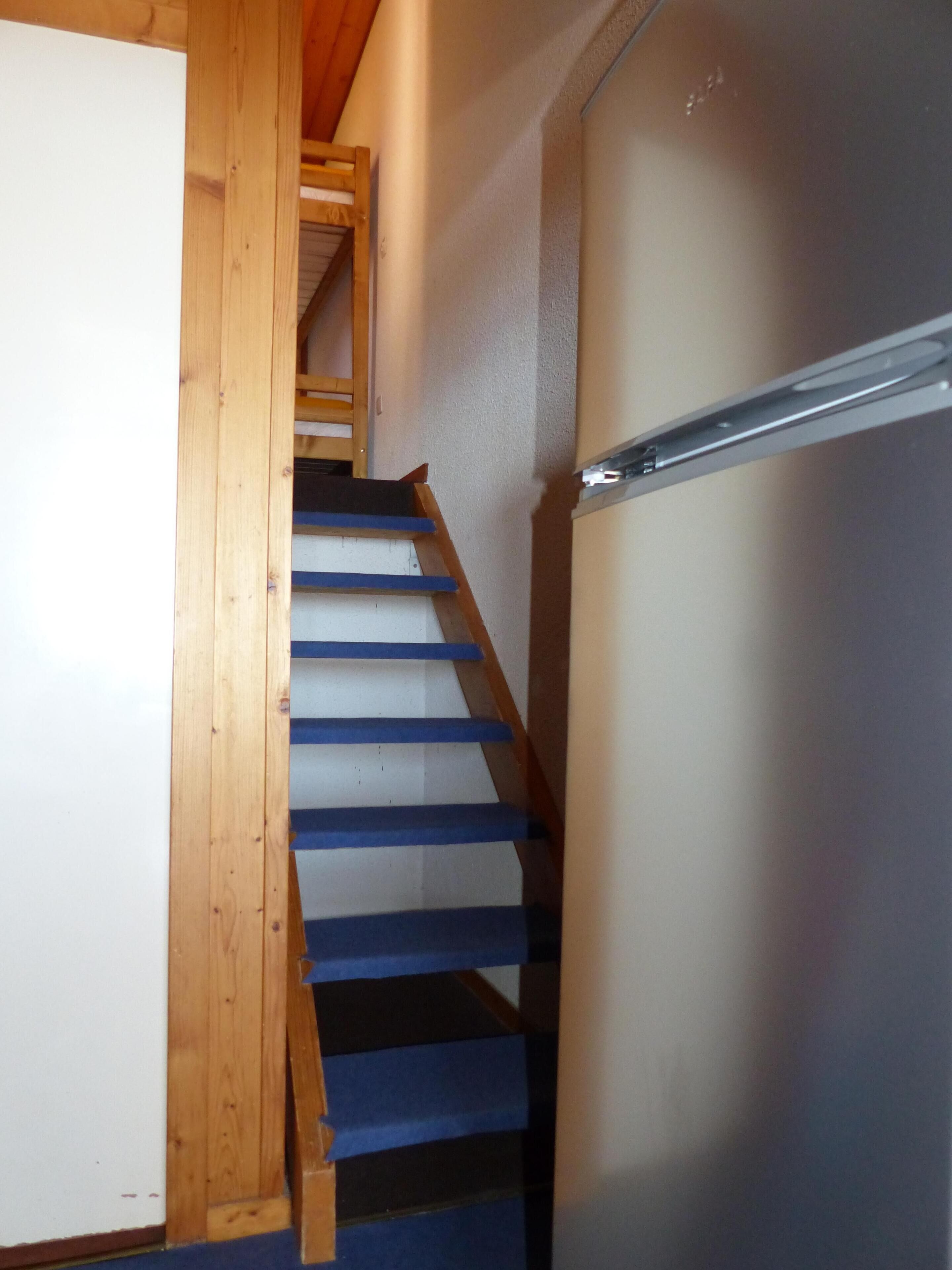 Un escalier en bois avec des marches bleues menant à un palier.