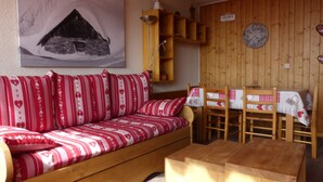 Una sala de estar acogedora con un sofá de madera, una mesa de comedor de madera con sillas, un aparador de madera y un reloj de pared.