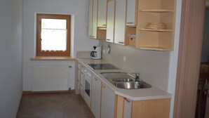 Kompakti keittiö, jossa on ikkuna, valkoiset kaapit, sisäänrakennettu uuni ja pesuallas.